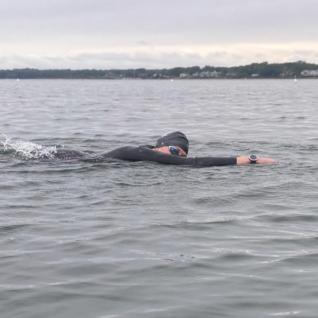 a wetsuit-clad swimmer riding high and flat in calm open water